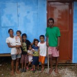 A family stands outside their completed house. The father of the family, despite having limited movement in his legs, completed the majority of the building work on his home by himself. The volunteers from the two schools aided with the painting and digging of a vegetable patch.